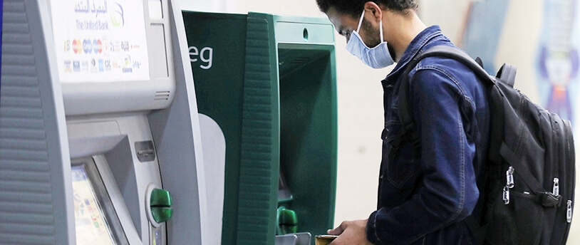 человек в маске снимает деньги с банкомата