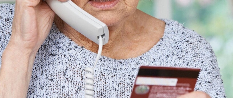 пожилая женщина разговаривает по телефону и держит в руках банковскую карту